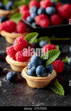 Petites tartelettes aux framboises fraîches et bleuets garnies de menthe sur fond noir. Banque D'Images