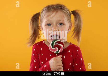 Portrait de fille mignonne léchant sucette sur fond orange Banque D'Images