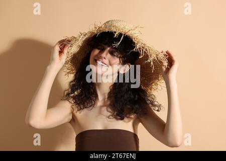 Belle femme heureuse portant un chapeau de paille au soleil sur fond beige. Accessoire de protection solaire Banque D'Images