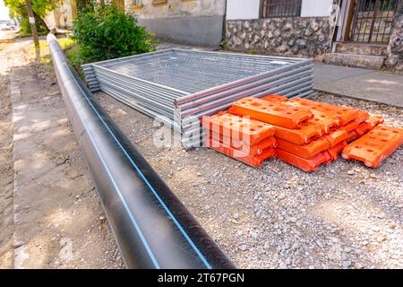 Pile, tas de pièces galvanisées pour les panneaux temporaires de clôture en métal sont empilés et pied creux de clôture en plastique sur la rue, prêt pour le montage autour de la construction Banque D'Images