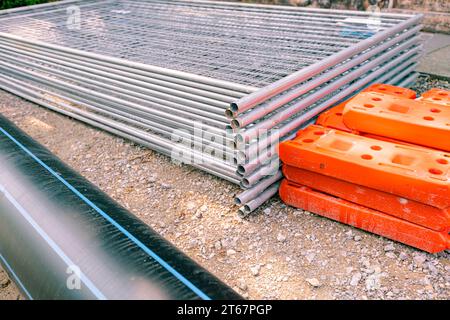 Pile, tas de pièces galvanisées pour les panneaux temporaires de clôture en métal sont empilés et pied creux de clôture en plastique sur la rue, prêt pour le montage autour de la construction Banque D'Images