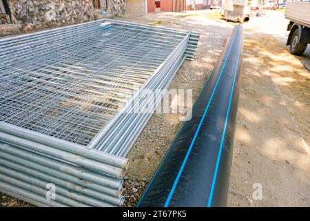 Pile, tas de pièces galvanisées pour les panneaux temporaires de clôture en fil métallique sont empilés sur la rue, prêts pour le montage autour du chantier de construction. Banque D'Images