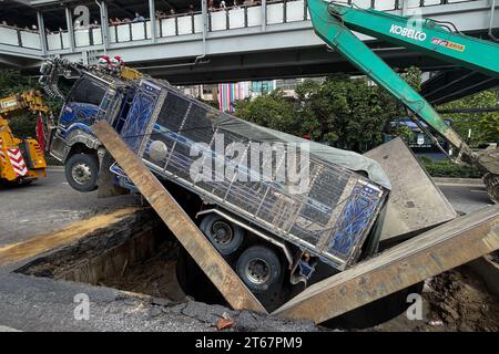 Un camion est assis dans une section de route effondrée après que le sol a cédé sous le poids du véhicule qui passait sur Sukwhumwit Road à Bangkok, Thaïlande, le 8 novembre 2023. Deux personnes ont été hospitalisées après l’incident survenu ce matin sur la route la plus fréquentée de Bangkok. Le camion transportait de la terre et de la boue provenant d'un chantier de construction lorsque les dalles de route en acier qui avaient servi à couvrir un tunnel sont tombées vers l'intérieur. L'accident a provoqué des embouteillages de plusieurs kilomètres pendant l'heure de pointe du déjeuner. Les spectateurs ont décrit un bang bruyant avant que le camion ne s'écrase à travers le sol. Deux motocycli Banque D'Images