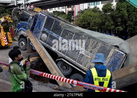 Un camion est assis dans une section de route effondrée après que le sol a cédé sous le poids du véhicule qui passait sur Sukwhumwit Road à Bangkok, Thaïlande, le 8 novembre 2023. Deux personnes ont été hospitalisées après l’incident survenu ce matin sur la route la plus fréquentée de Bangkok. Le camion transportait de la terre et de la boue provenant d'un chantier de construction lorsque les dalles de route en acier qui avaient servi à couvrir un tunnel sont tombées vers l'intérieur. L'accident a provoqué des embouteillages de plusieurs kilomètres pendant l'heure de pointe du déjeuner. Les spectateurs ont décrit un bang bruyant avant que le camion ne s'écrase à travers le sol. Deux motocycli Banque D'Images