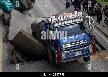 Un camion est assis dans une section de route effondrée après que le sol a cédé sous le poids du véhicule qui passait sur Sukwhumwit Road à Bangkok, Thaïlande, le 8 novembre 2023. Deux personnes ont été hospitalisées après l’incident survenu ce matin sur la route la plus fréquentée de Bangkok. Le camion transportait de la terre et de la boue provenant d'un chantier de construction lorsque les dalles de route en acier qui avaient servi à couvrir un tunnel sont tombées vers l'intérieur. L'accident a provoqué des embouteillages de plusieurs kilomètres pendant l'heure de pointe du déjeuner. Les spectateurs ont décrit un bang bruyant avant que le camion ne s'écrase à travers le sol. Deux motocycli Banque D'Images