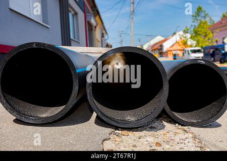 Peu de nouvelles conduites d'eau en plastique sont empilées sur la rue, prêtes à être placées dans la tranchée sur le site de construction. Banque D'Images