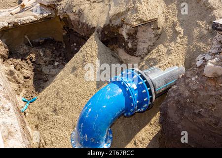 Accouplement avec des boulons pour connecter la grande plomberie, tuyau en plastique avec coude métallique de l'alimentation en eau souterraine de pipeline. Projet inachevé, tranchée non enterrée Banque D'Images