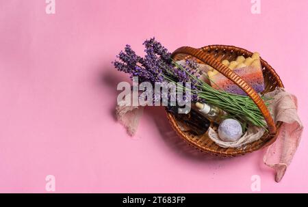 Fleurs de lavande fraîches, huile essentielle en bouteilles, sel de bain lavande et éponge de bain dans un petit panier en osier sur fond rose pastel. Avec copie s Banque D'Images