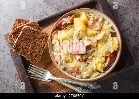 Chou cuit avec pommes de terre, saucisse, bacon et oignons gros plan dans un bol sur la table. Vue de dessus horizontale Banque D'Images