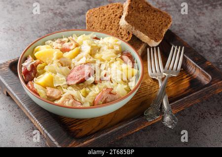 Chou cuit avec pommes de terre, saucisse, bacon et oignons gros plan dans un bol sur la table. Horizontal Banque D'Images