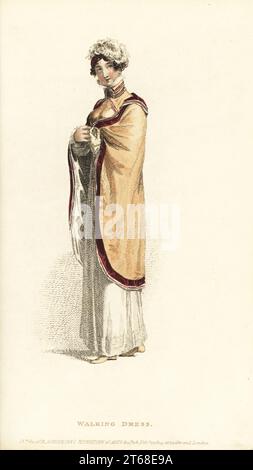 Regency femme en robe de promenade.Robe ronde haute de couleur camourique, manteau russe de saumon pâle, bordée de velours morone et de fil de soie blanc, spencer bodice, petit chapeau de casque avec plumes d'autruche, demi-bottes, gants d'enfant citron.Plaque 12, vol. 10, le 1 février 1814.Gravure sur plaque de coperplate de couleur main de Rudolph Ackermann's Repository of Arts, Londres. Banque D'Images