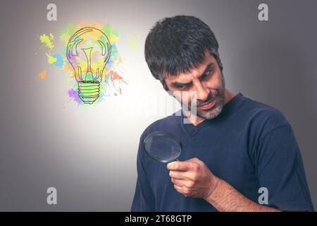 Un homme mûr se tient sur un fond blanc tout en examinant une loupe dans ses mains Banque D'Images