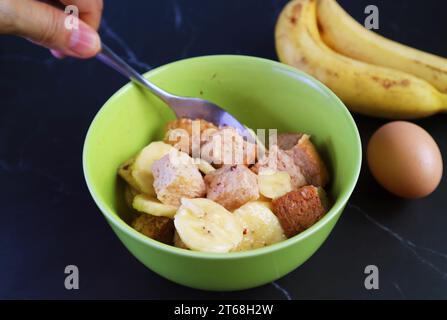 Mélanger les ingrédients à la main dans un bol à mélanger pour cuire le pudding de pain de banane Banque D'Images