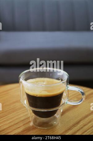 Tasse de café chaud dans une tasse transparente avec canapé flou en arrière-plan Banque D'Images