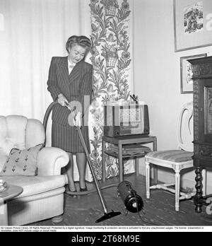 Passer l'aspirateur dans les années 1940 Une femme habillée dans une tenue typique des années 1940 est vue aspirer la moquette dans le salon. Suède 1945. Kristoffersson réf. L178-3 Banque D'Images