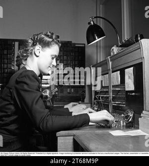 Une jeune femme travaille au standard de l'entreprise 1942. Elle connecte les appels entrants et sortants à la bonne personne en utilisant des cordons pour les téléphones respectifs dans un soi-disant commutateur de cordon. La coiffure est typique des années 1940 Suède en 1942. Kristoffersson réf. A120-1 Banque D'Images