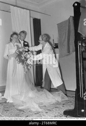 S'embrasser dans les années 1940 Couple de jeunes mariés Rohlsson ayant leur photo de mariage prise par un photographe professionnel dans un studio qui fait quelques ajustements aux arrangements floraux avant qu'il ne prenne les photos. Suède 1941 Kristoffersson Ref 199-16 Banque D'Images