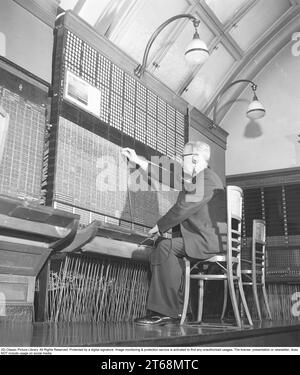 Central téléphonique. Un homme est assis à un standard manuel. Tous les appels entrants et sortants doivent être connectés et il le fait en branchant le cordon et la fiche à la bonne connexion. Le standard téléphonique est un objet de musée du tournant du siècle 1800-1900 et l'homme démontre sa fonction. Suède 1953. Kristoffersson réf. BM23-6 Banque D'Images