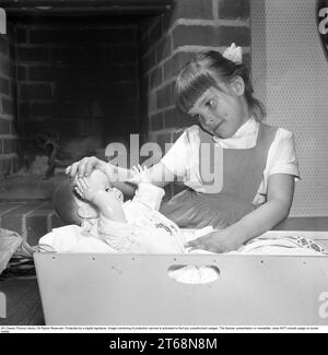 Une fille avec une poupée dans les années 1950 Une petite fille joue avec sa poupée. Elle tient sa main sur le front de la poupée comme une mère le sentirait si son enfant avait chaud et avait de la fièvre. Suède 1956. Kristoffersson réf. BS39-9 Banque D'Images