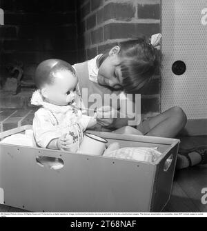 Une fille avec une poupée dans les années 1950 Une petite fille joue avec sa poupée. Elle met une cuillère à sa bouche comme vous le faites quand vous donnez à un enfant leur médicament. Suède 1956. Kristoffersson réf. BS40-5 Banque D'Images