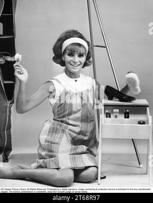 Dans les années 1960 Une femme a vu polir des chaussures avec le vernis et le pinceau visibles, habillés d'un tablier typique des années 1960. Suède 1963. Banque D'Images
