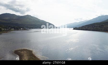 Vue aérienne d'un lac tranquille entouré de montagnes verdoyantes en arrière-plan, soulignant la beauté naturelle du paysage Banque D'Images
