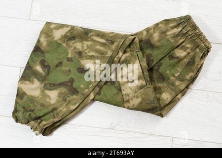 Gros plan pantalon Camouflage sur fond en bois, pantalon kaki vert. Pantalon élastique soldat de camouflage déplié sur fond en bois. Banque D'Images
