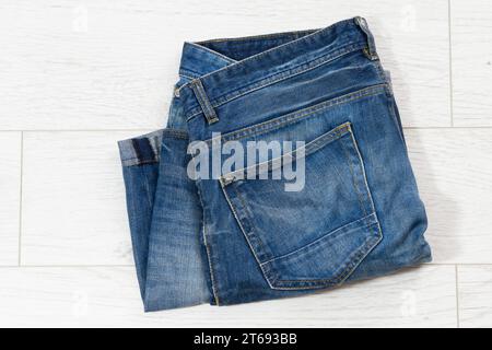 Jeans bleus pliés sur fond en bois blanc, denim plié sur fond en bois clair - vue de dessus Banque D'Images