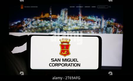 Personne tenant un téléphone portable avec le logo de la société philippine San Miguel Corporation (SMC) devant la page Web de l'entreprise. Concentrez-vous sur l'affichage du téléphone. Banque D'Images