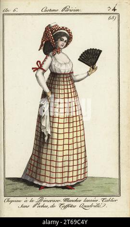 Femme dans les modes de 1798. Elle porte un chapeau de style Primerose attaché avec un fichu à carreaux. Sa robe a des manches lacées, et son tablier sans poche est en taffetas à carreaux. Elle tient un éventail et un mouchoir. Le chapeau peut être inspiré par le costume d'un paysan provençal joué par Madame St. Aubin dans l'opéra Primerose de Nicolas Dalayracs qui a débuté en 1798. Chapeau à la primerose. Manches Lassees. Tablier sans poches de taffetas quadrille. Gravure sur cuivre coloriée à la main de Pierre de la Mesangeres Journal des modes et Dames, Paris, 1798. Les illustrations du volume 1 sont de Carle Vernet, Claude Louis de Banque D'Images
