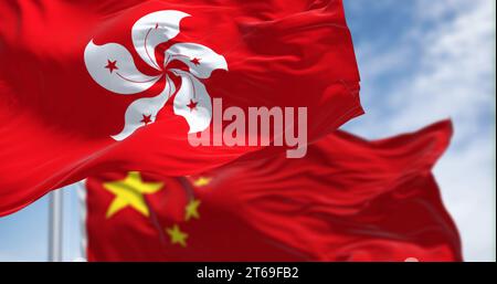 Drapeaux de Hong Kong et de Chine agitant dans le vent par temps clair. Hong Kong est une ville et une région administrative spéciale en Chine. Tissu ondulé. Sél Banque D'Images