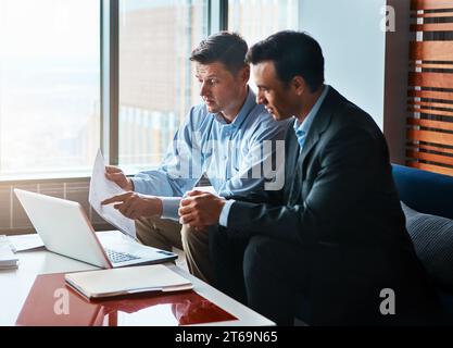 Passons-le en revue ensemble. deux hommes d'affaires discutant assis près d'un ordinateur portable. Banque D'Images