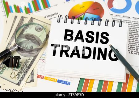 Concept commercial. Sur la table sont des graphiques d'affaires, des dollars et un bloc-notes avec l'inscription - Basis Trading Banque D'Images