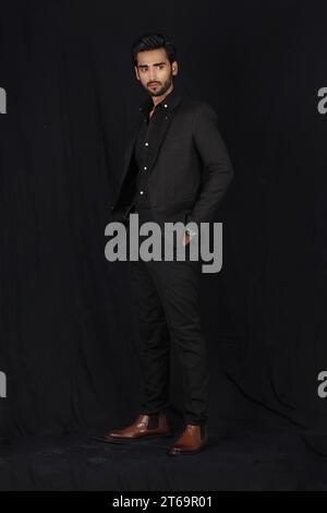 Portrait de beau jeune homme d'affaires en costume élégant posant sur fond noir Banque D'Images