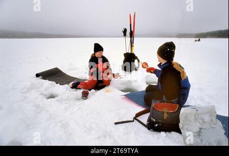 TROMSO, NORVÈGE - JANVIER 14 2022 : pêcheurs pêchant sur glace sur un lac gelé en hiver avec canne à pêche ou canne à pêche, tarière à glace et équipement pour la pêche Banque D'Images