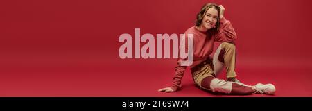 bannière de femme joyeuse en pantalon patchwork et manches longues court assis sur fond rouge Banque D'Images