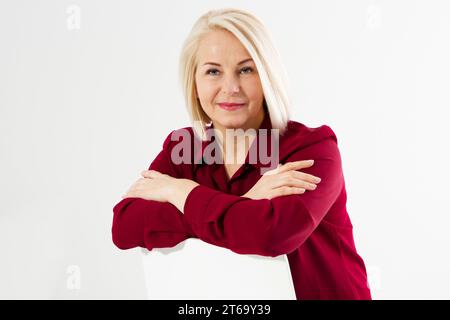 Portrait de souriante joyeuse femme blonde d'âge moyen assise sur une chaise isolée sur blanc Banque D'Images