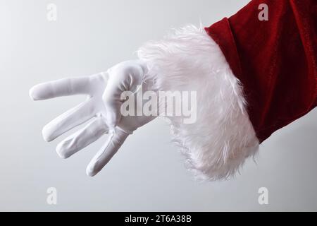 Détail de la main du père noël montrant quatre doigts avec des gants blancs traditionnellement habillés en rouge isolé avec fond dégradé derrière. Banque D'Images