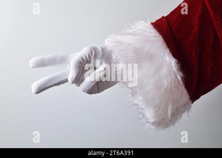 Détail de la main du père noël montrant deux doigts avec des gants blancs traditionnellement habillés en rouge isolé avec fond dégradé derrière. Banque D'Images