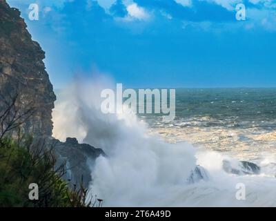 Un magnifique paysage marin avec des vagues qui s'écrasent sur une plage rocheuse, avec de grands rochers déchiquetés et des arbres verdoyants en arrière-plan Banque D'Images