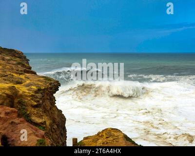 Une plage tropicale pittoresque avec des vagues bleues cristallines tapant sur le sable blanc, sous un décor spectaculaire de falaises verdoyantes et d'arbres Banque D'Images