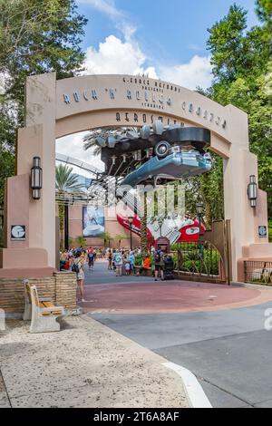 Les clients du parc masqué sortent sous le panneau d'entrée pour le Rock 'n' Roller Coaster Ride au parc thématique Disney's Hollywood Studios Banque D'Images