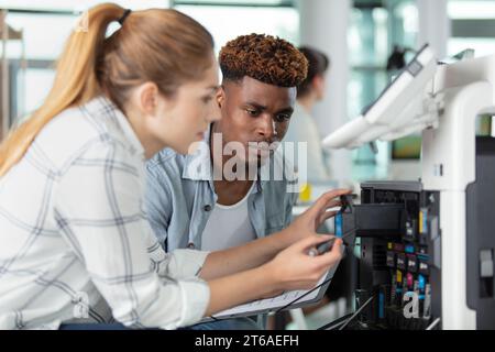 homme regardant la femme remplacer la cartouche d'encre dans l'imprimante industrielle Banque D'Images