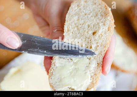 Gros plan des mains d'une femme étalant du beurre sur une tranche de pain. Restauration rapide pour la randonnée ou si vous n'avez pas le temps de faire de la nourriture. Banque D'Images