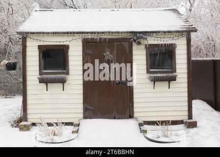 Blanc crémeux avec cabanon de jardin de garniture brune couvert de glace dans la cour arrière après une tempête de pluie gelée au début du printemps. Banque D'Images