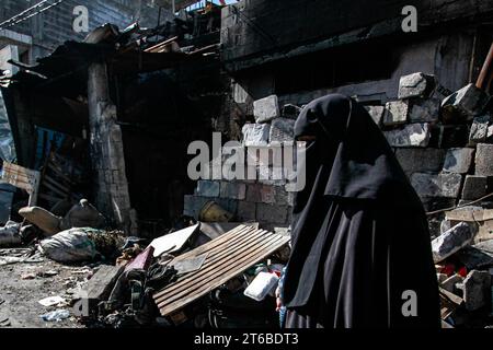 Une palestinienne vue marche près d’un bâtiment bombardé dans une rue détruite après un raid militaire israélien dans le camp de réfugiés de Tulakrem en Cisjordanie. Banque D'Images