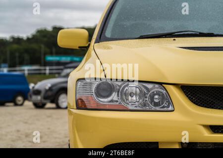 Chester, Cheshire, Angleterre, 30 septembre 2023. Gros plan d'un phare Mitsubishi EVO VIII jaune avec gouttes de pluie sur la peinture. Banque D'Images