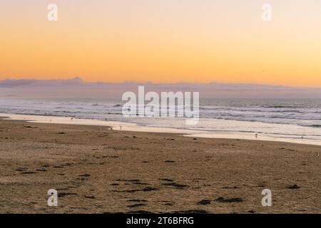 Un coucher de soleil à couper le souffle sur la plage peint le ciel dans de superbes teintes de jaune, projetant une lueur chaleureuse et sereine sur la scène tranquille Banque D'Images