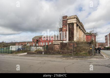 Burslem, Stoke on Trent, Angleterre, 21 mars 2023. Couple âgé marchant devant les ruines de l'école du dimanche avec l'usine de poterie fermée de Wade en arrière-plan. Banque D'Images