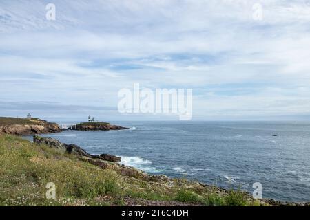 littoral avec un phare sur une petite île, un bateau dans l'eau, et un ciel bleu avec des nuages blancs Banque D'Images